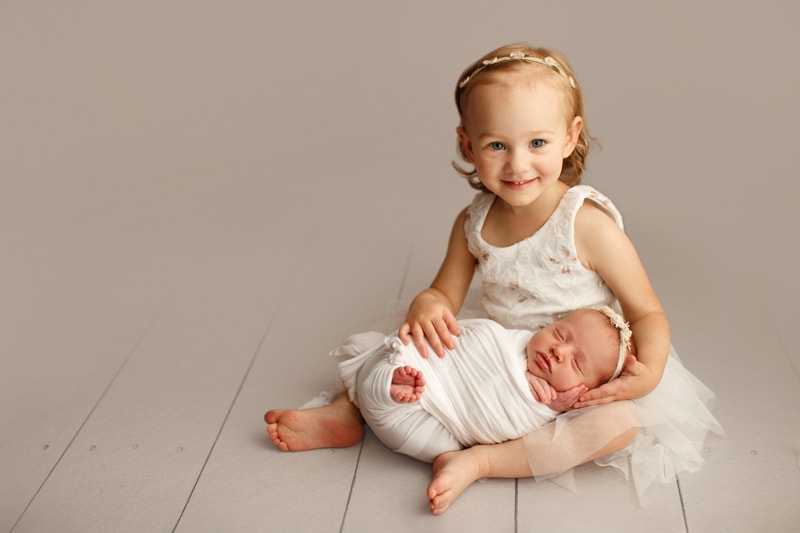 Big sister holding her swaddled newborn sibling at the hospital bedside