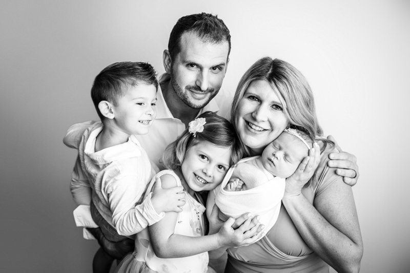 Black and white portrait of parents and two siblings holding their swaddled newborn
