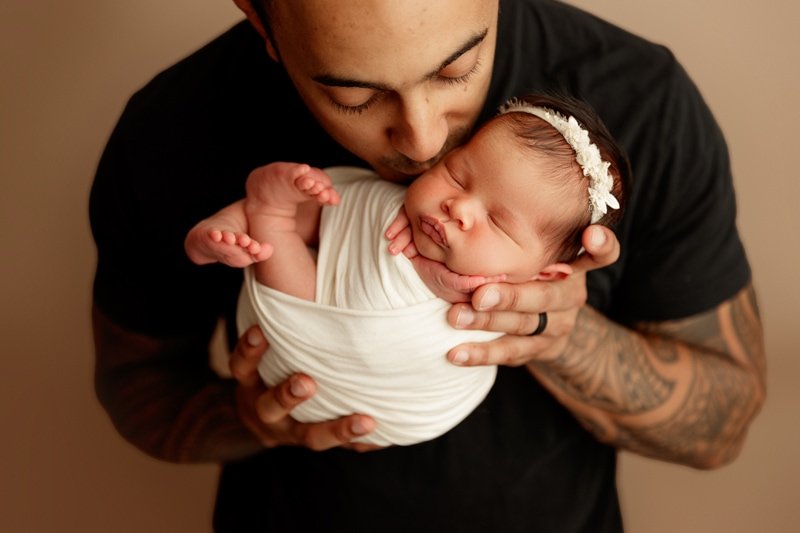 Father kissing his swaddled newborn daughter's forehead