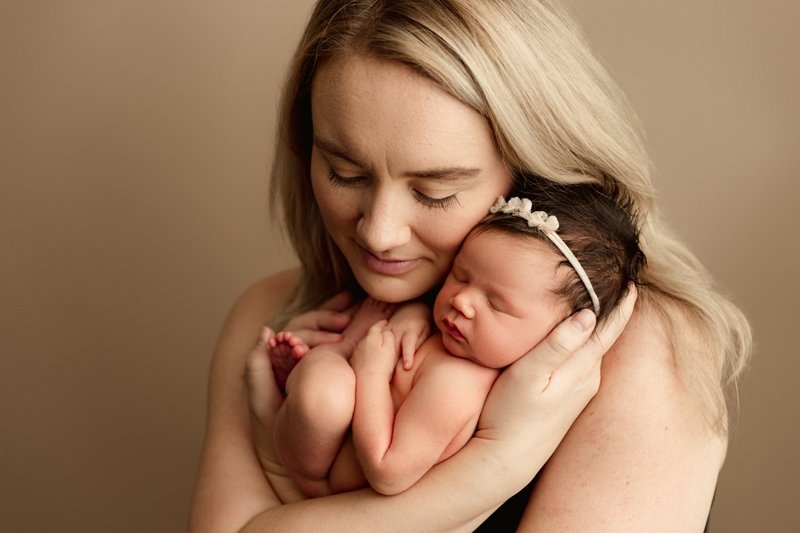 Mother cuddling her newborn daughter cheek to cheek