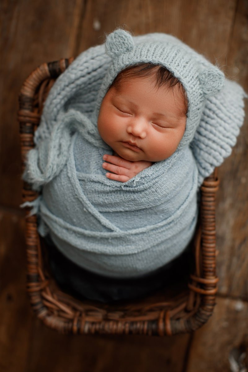 Newborn in a blue knit bear bonnet asleep in a basket