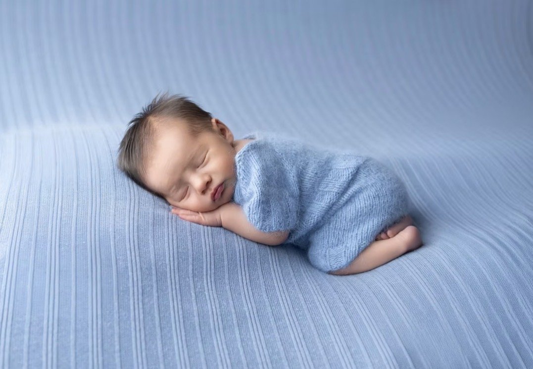 Newborn in a blue knit romper asleep on a soft blue blanket