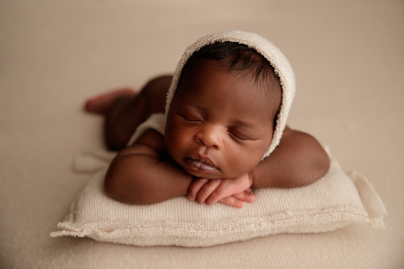 Newborn in a cream bonnet asleep on a pillow, in-hospital portrait