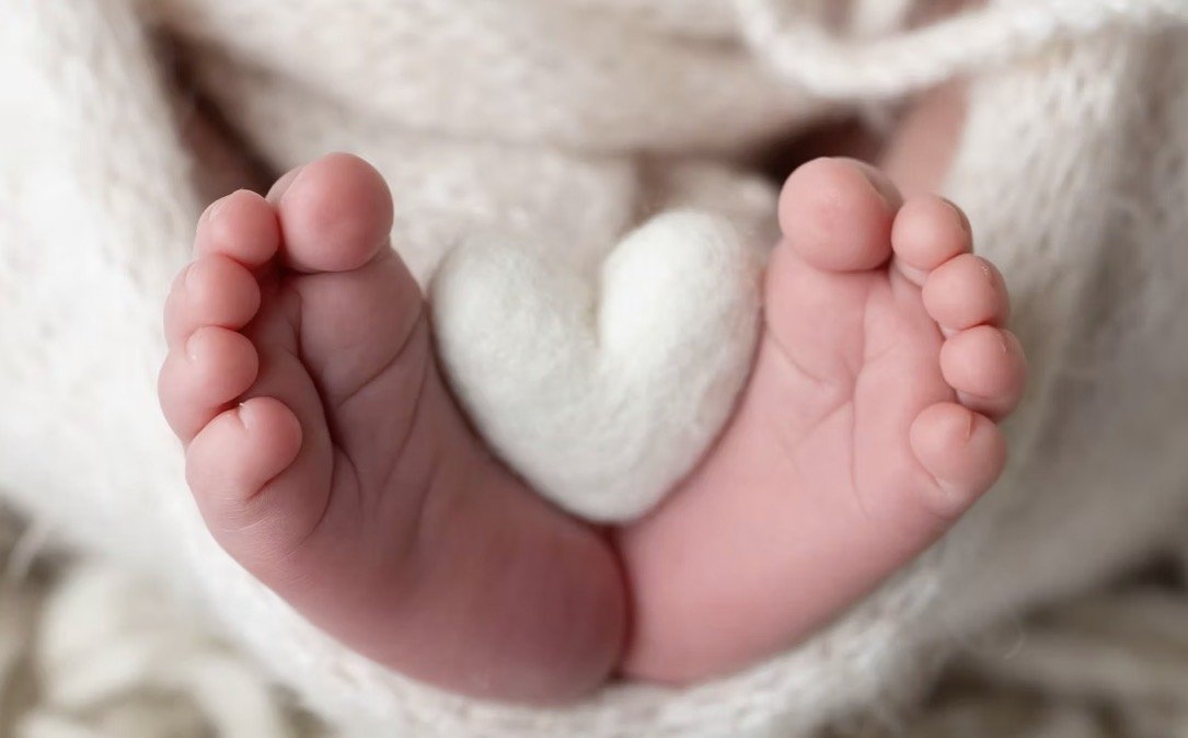 Newborn feet holding a white felt heart