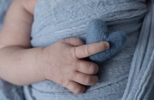 Newborn hand holding a small felt heart