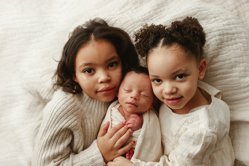 Two big sisters cuddling their sleeping newborn sibling